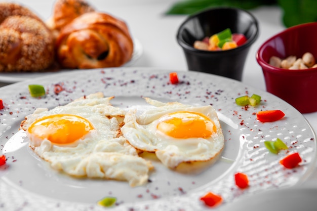 Oeufs au plat dans une assiette avec une pâtisserie en arrière-plan. vue de dessus.