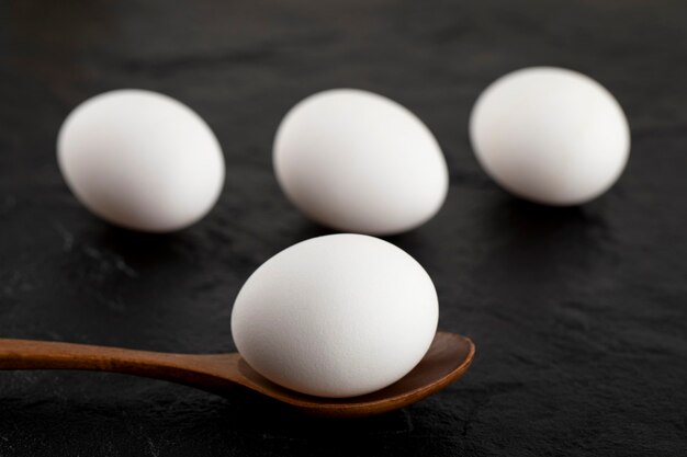 Oeufs blancs crus et cuillère en bois sur une surface noire.