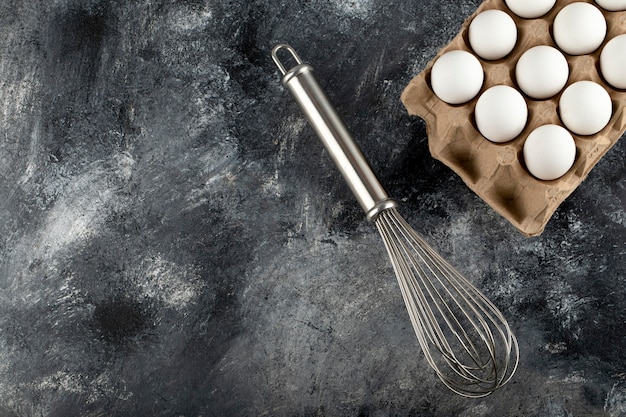 Oeufs blancs dans un contenant en carton et moustaches sur une surface en marbre.