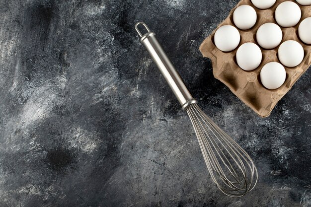 Oeufs blancs dans un contenant en carton et moustaches sur une surface en marbre.