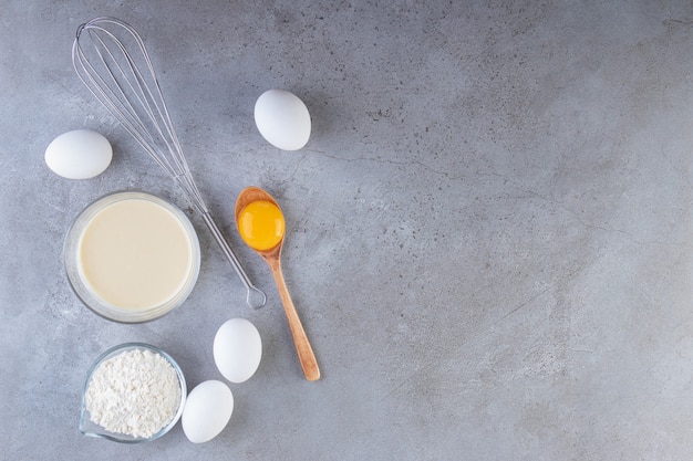 Oeufs blancs, jaune et bol de farine sur table en pierre.