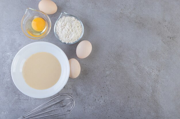 Oeufs blancs, jaune et bol de farine sur table en pierre.