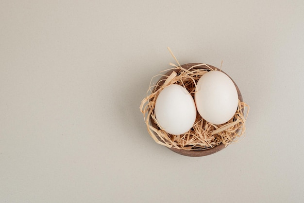 Oeufs blancs de poulet frais avec du foin dans un bol en bois.