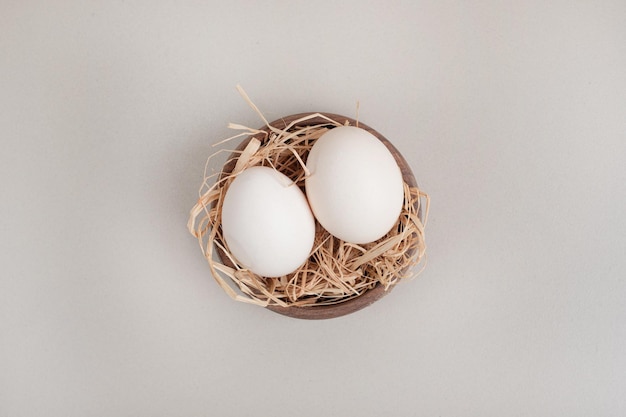 Oeufs blancs de poulet frais avec du foin dans un bol en bois.