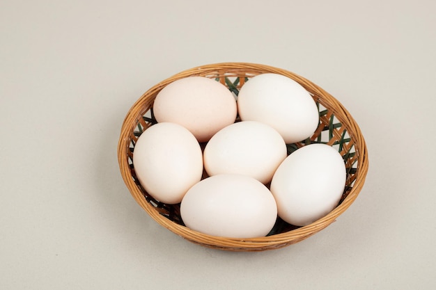 Oeufs blancs de poulet frais sur panier en osier.