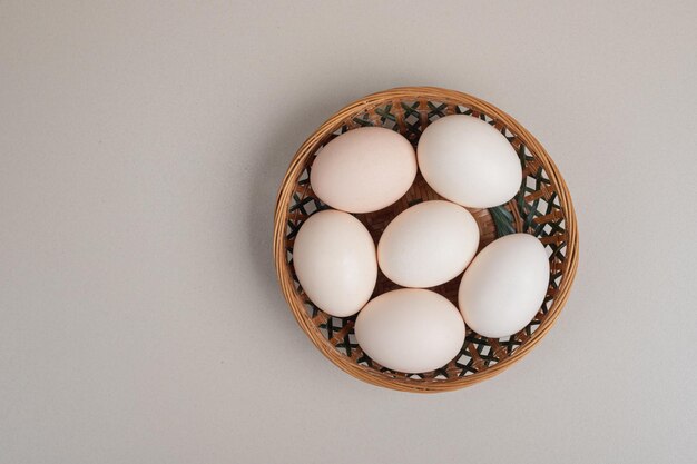 Oeufs blancs de poulet frais sur panier en osier.