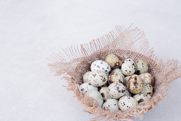 Oeufs de caille bio dans un bol sur une surface blanche.