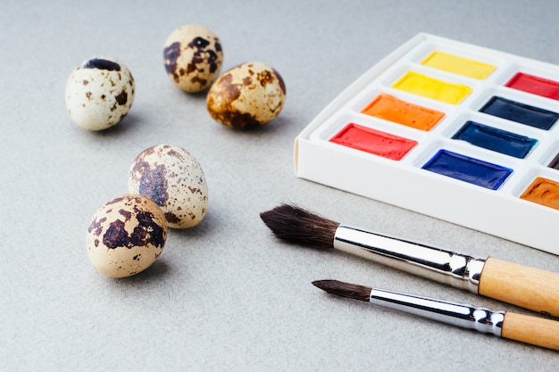 Oeufs à colorier pour pâques. peintures, pinceaux, œufs de caille sur fond gris. préparation pour la célébration de pâques, décorations traditionnelles, arrière-plan. concept créatif.