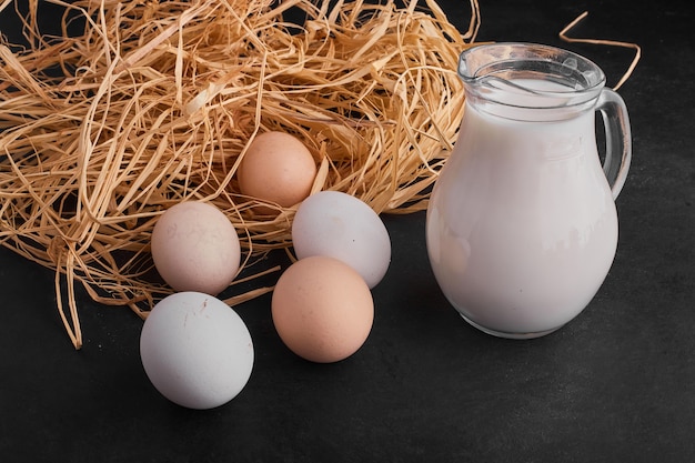 Oeufs dans le nid sur une surface noire avec un pot de lait de côté.