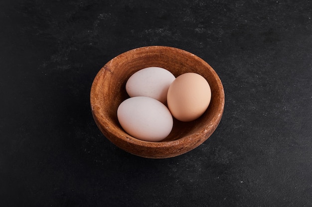 Oeufs dans une tasse en bois sur un espace noir.