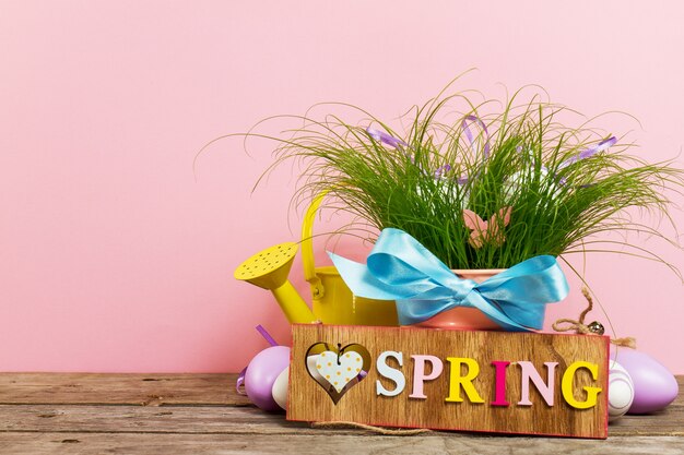 Oeufs décoratifs colorés dans un pot de fleurs avec de l&#39;herbe verte fraiche sur une table en bois sur fond rose. Horizontal avec espace de copie.