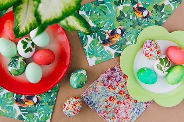 Photo gratuite oeufs de pâques sur des assiettes près de serviettes avec des peintures tropicales