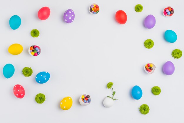 Oeufs de Pâques avec des bonbons et des fleurs dispersés sur une table blanche