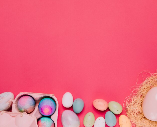 Oeufs de Pâques colorés dans le carton et nid sur le fond de fond rose