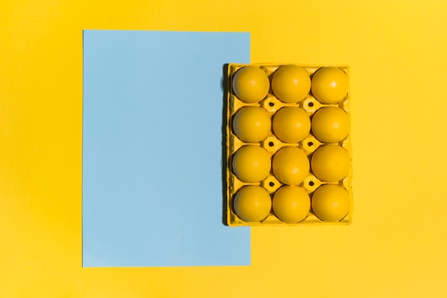 Photo gratuite oeufs de pâques colorés en rack avec une feuille de papier vierge sur la table