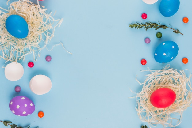 Oeufs de Pâques dans les nids avec des branches de plantes et des bonbons sur la table