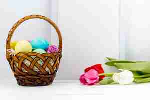 Photo gratuite oeufs de pâques dans le panier avec des tulipes et un cadre vide sur la table