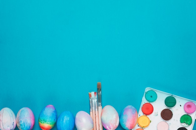 Oeufs de pâques peints; pinceaux et boîte de peinture aquarelle sur le fond bleu avec espace de copie