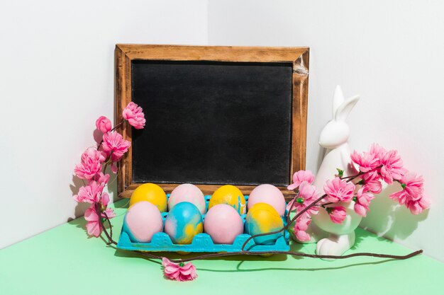 Oeufs de Pâques en rack avec tableau blanc et fleurs sur la table