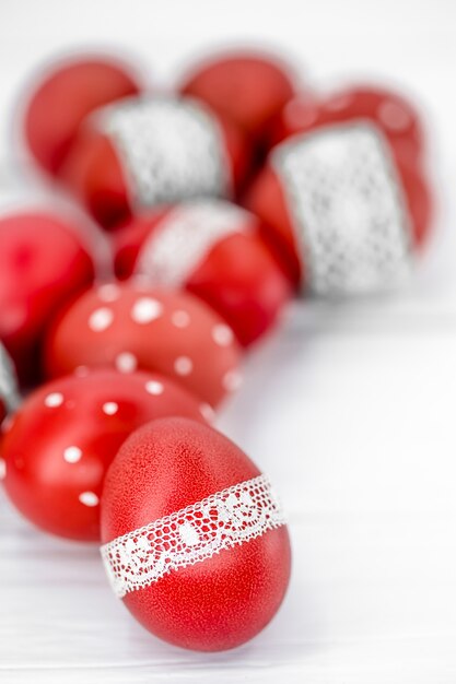 Oeufs de Pâques rouges sur ruban de dentelle attaché blanc, gros plan, couché sur un bois blanc