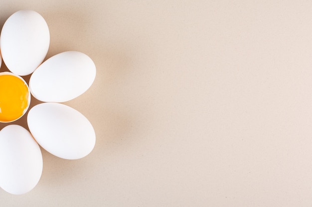 Oeufs de poule blancs crus frais placés sur une table beige.