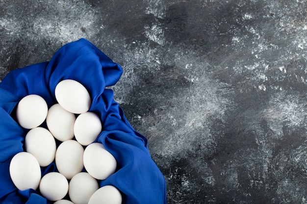 Photo gratuite oeufs de poule crus blancs avec sur une nappe bleue.