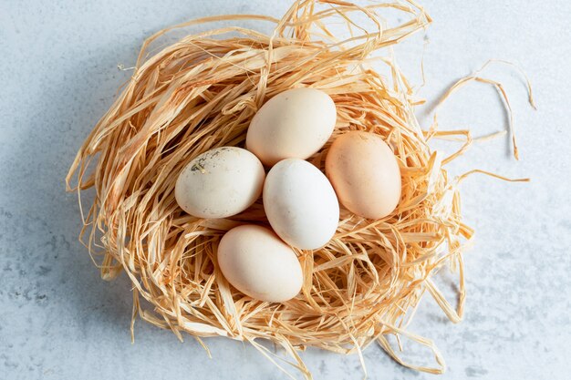 Oeufs de poule frais dans de la paille sur une surface grise.