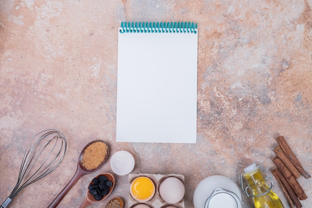 Photo gratuite Œufs de poule, lait, huile et cahier sur une surface en marbre.