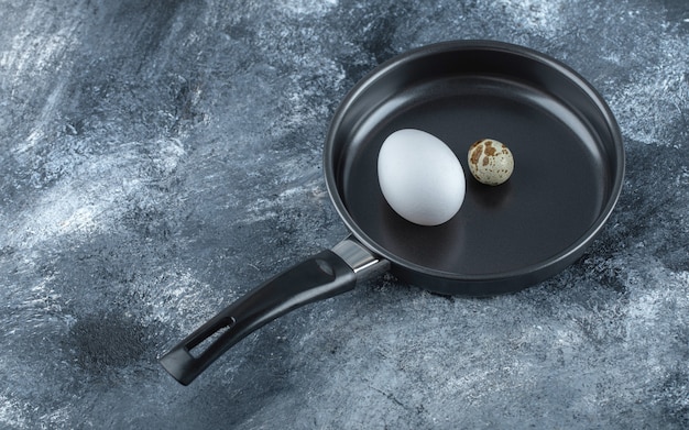 Oeufs de poulet et de caille biologiques frais dans une poêle à frire noire.