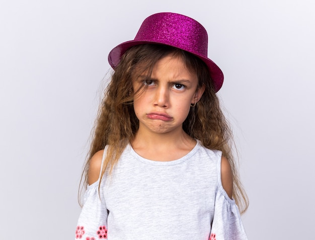 offensé petite fille caucasienne avec chapeau de fête violet isolé sur mur blanc avec espace de copie