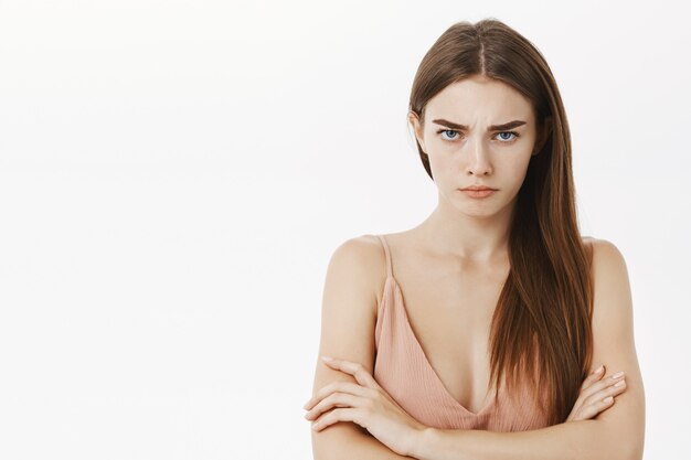 Offensé sombre et bouleversé jolie jeune femme croisant les bras contre la poitrine en posture défensive debout mécontent et intense