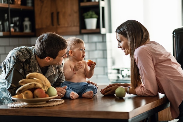 Un officier militaire heureux et sa femme passent du temps avec leur bébé qui mange des fruits à la maison