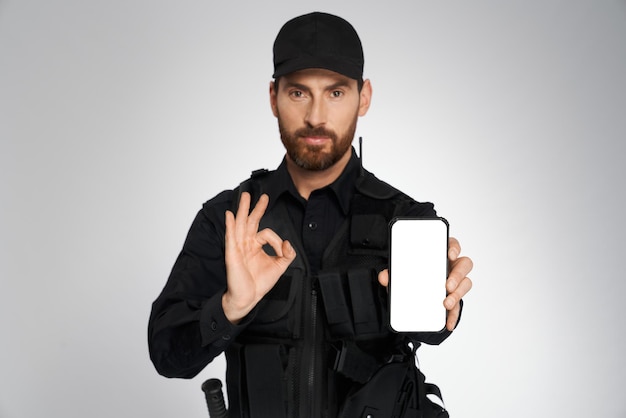 Officier de police masculin sérieux montrant un écran de téléphone portable vide avec un portrait de lieu de copie de barbu