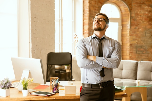 Photo gratuite offres. un jeune homme d'affaires travaillant au bureau, obtenant un nouveau lieu de travail. jeune employé de bureau masculin tout en gérant après la promotion. ça a l'air sérieux, confiant. affaires, style de vie, nouveau concept de vie.