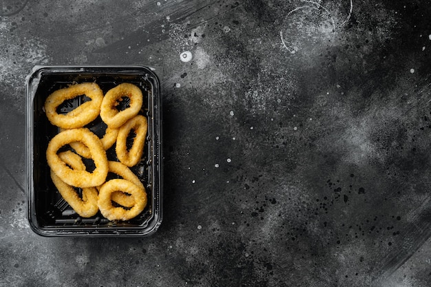 Oignon frit croustillant brut ou anneau de calamars en plastique, sur fond de table en pierre noire foncée, vue de dessus à plat, avec espace de copie pour le texte