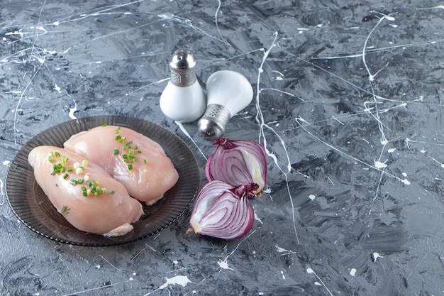 Photo gratuite oignon tranché et poitrine de poulet sur une assiette , sur le fond de marbre.