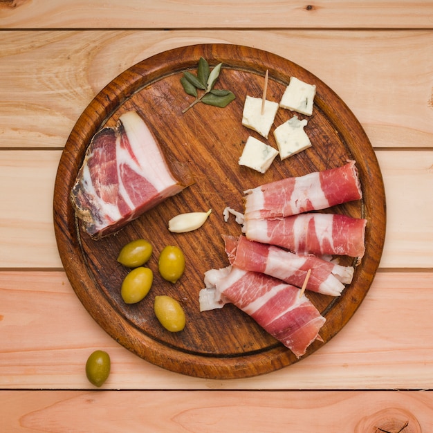 Olives; gousse d&#39;ail; tranche de fromage et bacon sur un plateau en bois au-dessus du bureau