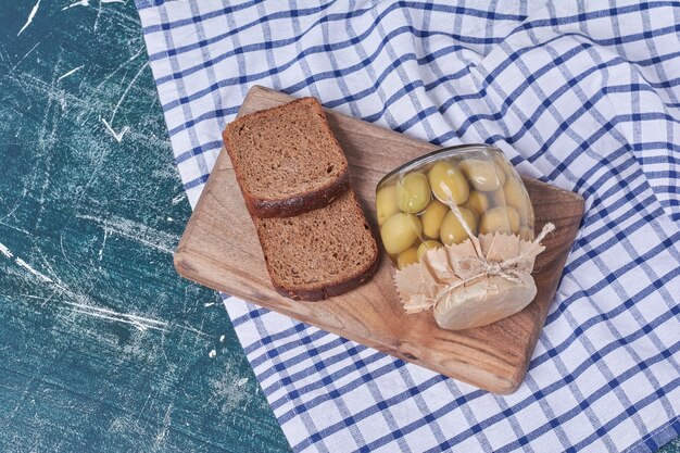 Olives marinées dans un bocal en verre avec des tranches de pain noir sur bleu.