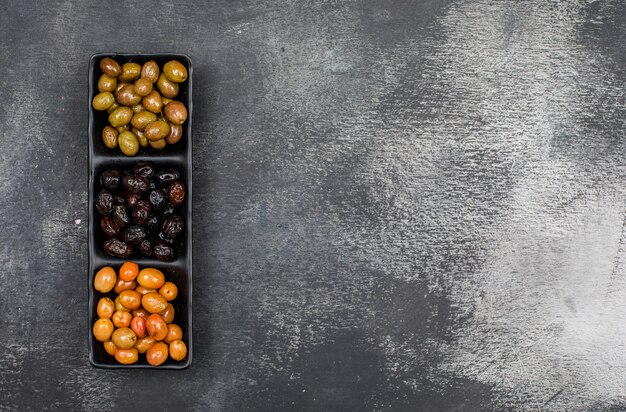 Olives marinées fraîches dans une assiette noire sur grunge gris foncé. vue de dessus.