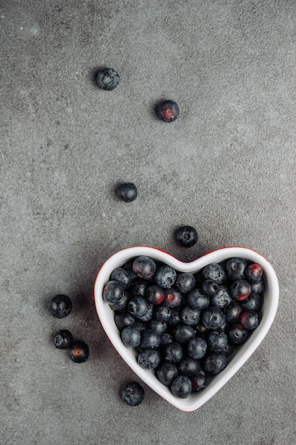 Olives noires dans un bol en forme de coeur sur fond gris. vue de dessus.