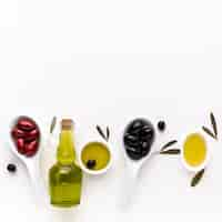 Photo gratuite olives noires rouges en cuillères avec bouteille d'huile