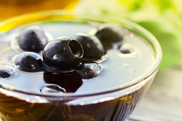 Des olives noires savoureuses fraîches et fraîches avec de l&#39;huile d&#39;olive sur un bol sur fond clair.
