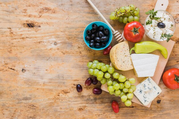 Olives, tomates, piment vert avec plateau de fromages sur table en bois