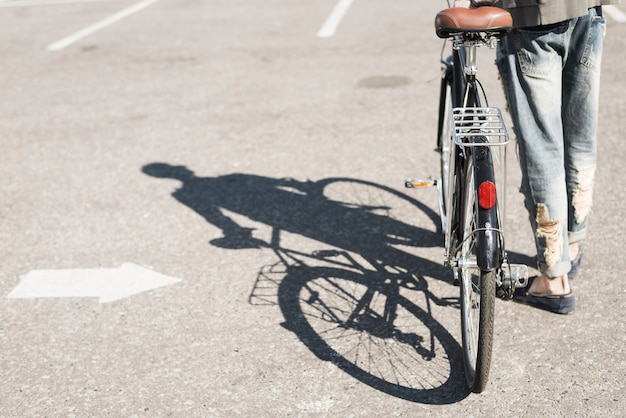 Photo gratuite ombre de l'homme marchant à vélo sur l'asphalte