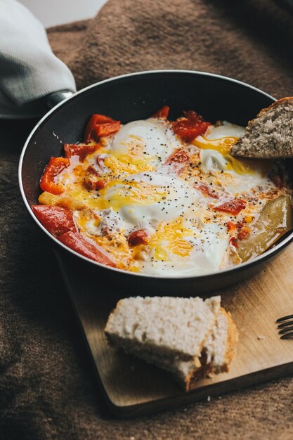 omelette au poivron rouge dans une casserole près de pain noir en tranches sur une planche de bois