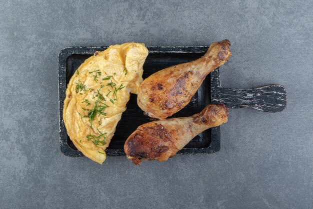 Omelette savoureuse et cuisses de poulet sur tableau noir.