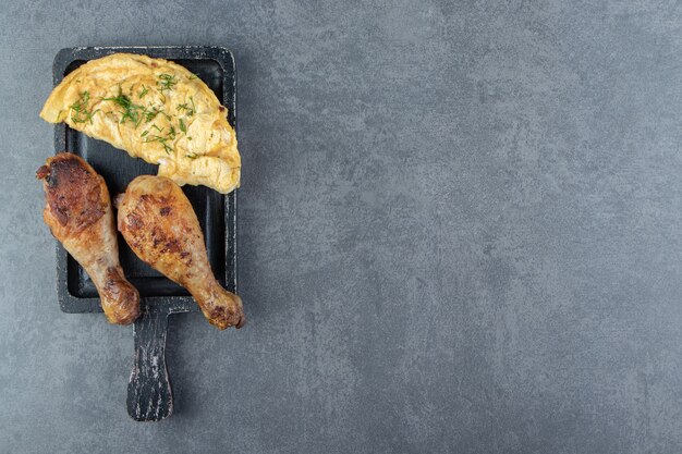 Omelette savoureuse et cuisses de poulet sur tableau noir.