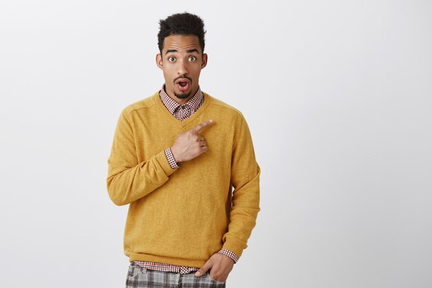 OMG, avez-vous entendu des nouvelles choquantes. Portrait de beau mec étonné à la peau sombre avec une coiffure afro pointant vers le coin supérieur droit et laissant tomber la mâchoire de surprise