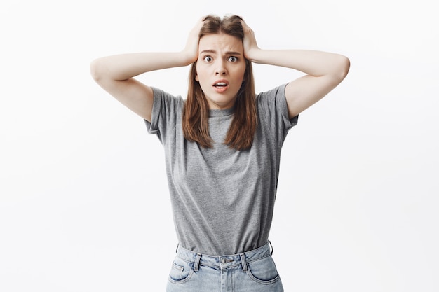 Photo gratuite omg. gros plan d'une belle jeune étudiante malheureuse aux cheveux noirs se tenant la main sur la tête, avec une expression effrayée se souvenant qu'elle n'avait pas éteint le fer à la maison.