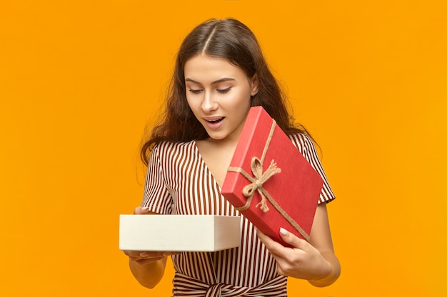 OMG. Jolie fille d'anniversaire portant du maquillage et une robe rayée élégante posant au mur blanc orange